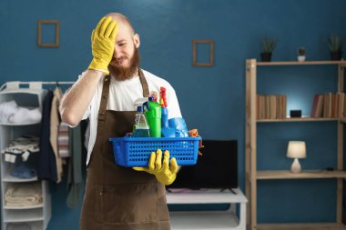 Eldiven giyen, eldiven takan, önlük tutan, temizlik malzemesi taşıyan yorgun bir adam. Stres ve depresyondan kafası ağrıyor. Ev işlerinde erkek hizmetçi. Boşluğu kopyala
