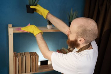 Kel adam evde temizlik yaparken toz ve kiri temizlemek için bez kullanıyor. Ev işleri, ev işleri, yaşam alanı için kişisel bakım ve günlük temizlik rutinini gösteriyor.