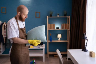 Profesyonel temizlik servisinden erkek hademe ev içi fırçayla yastık fırçalıyor. Ev işleri ve ev idaresi kavramı.