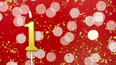 Altın yanan mum bir numara. Kırmızı arkaplanda 1 yazılı doğum günü tebrik kartı konfeti ve simle. Yıldönümü, kutlama etkinliği ve doğum günü konsepti.