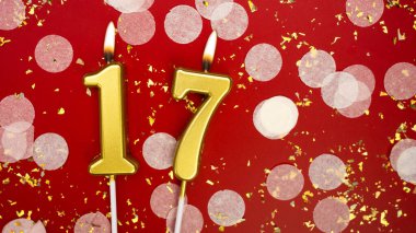 Altın yanan mum numarası 17. Kırmızı arkaplanda 17 yazılı doğum günü tebrik kartı konfeti ve simle. Yıldönümü, kutlama etkinliği ve doğum günü konsepti.
