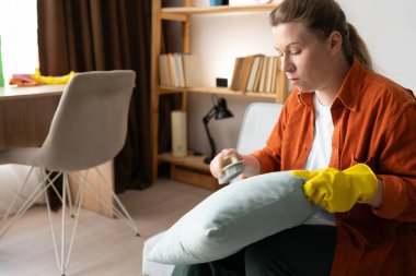 Kanepede oturan kadın temizlik fırçasıyla yastığı fırçalıyor. Ev temizlik rutinini, tekstil bakımını, günlük işleri ve ev işleri ve ev işleri kavramını gösteriyor.