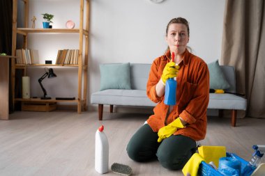 Comic woman wearing yellow gloves sitting on floor with cleaning supplies and detergents, showing dumb fish lips. Home cleaning, household, housekeeping and housework concept.