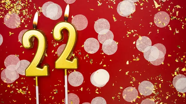 Altın yanan mum numarası 22 'dir. Kırmızı arkaplanda 22. yazıyla birlikte konfeti ve simle birlikte doğum günü tebrik kartı. Yıldönümü, kutlama etkinliği ve doğum günü konsepti.