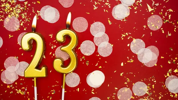 Altın yanan mum numarası yirmi üç. Kırmızı arka planda 23 yazısıyla birlikte konfeti ve simle birlikte doğum günü tebrik kartı. Yıldönümü, kutlama etkinliği ve doğum günü konsepti.
