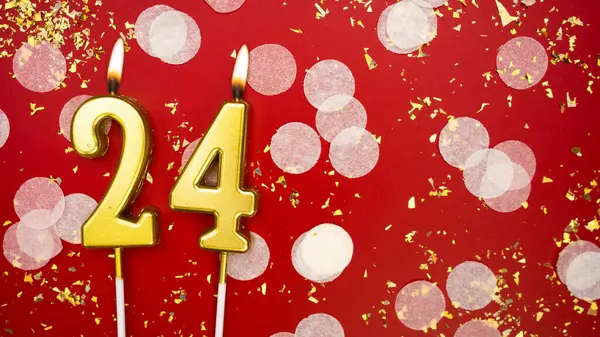 Altın yanan mum numarası 24 numara. Kırmızı arkaplanda 24 yazılı doğum günü tebrik kartı konfeti ve simle. Yıldönümü, kutlama etkinliği ve doğum günü konsepti.