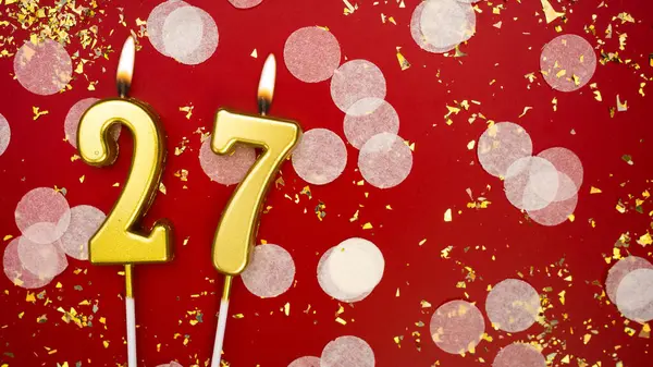 Altın yanan mum numarası yirmi yedi. Kırmızı arkaplanda 27 yazılı doğum günü tebrik kartı konfeti ve simle. Yıldönümü, kutlama etkinliği ve doğum günü konsepti.
