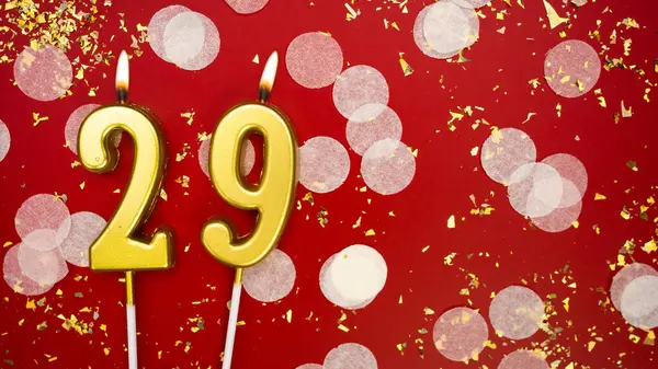 Altın yanan mum numarası 29 'du. Kırmızı arkaplanda 29 yazısıyla birlikte konfeti ve simle doğum günü tebrik kartı. Yıldönümü, kutlama etkinliği ve doğum günü konsepti.