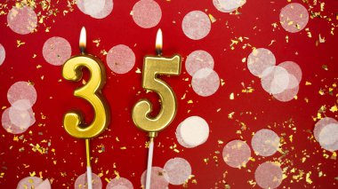 Altın yanan mum numarası 35 numara. Kırmızı arkaplanda 35 yazılı doğum günü tebrik kartı konfeti ve simle. Yıldönümü, kutlama etkinliği ve doğum günü konsepti.