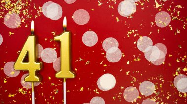 Kırk bir numaralı altın yanan mum. Kırmızı arka planda 41 yazısıyla konfeti ve simle birlikte doğum günü tebrik kartı. Yıldönümü, kutlama etkinliği ve doğum günü konsepti.