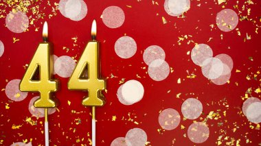 Kırk dört numaralı altın yanan mum. Kırmızı arka planda 44 yazısıyla birlikte konfeti ve simle birlikte doğum günü tebrik kartı. Yıldönümü, kutlama etkinliği ve doğum günü konsepti.