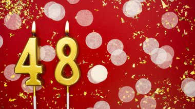Kırk sekiz numaralı altın yanan mum. Kırmızı arkaplanda 48 yazılı konfeti ve simle doğum günü tebrik kartı. Yıldönümü, kutlama etkinliği ve doğum günü konsepti.