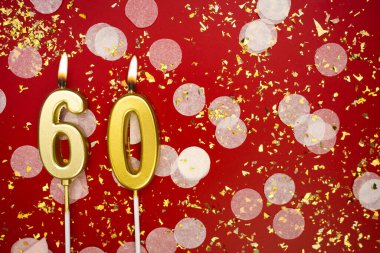 Altın yanan mum numarası altmış. Kırmızı arkaplanda 60 yazılı doğum günü tebrik kartı konfeti ve simle. Yıldönümü, kutlama etkinliği ve doğum günü konsepti.
