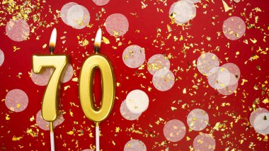 Yanan altın mum numarası 70. Kırmızı arkaplanda 70 yazılı doğum günü tebrik kartı konfeti ve simle. Yıldönümü, kutlama etkinliği ve doğum günü konsepti.