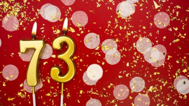 Altın yanan mum numarası yetmiş üç. Kırmızı arkaplanda 73 yazılı doğum günü tebrik kartı konfeti ve simle. Yıldönümü, kutlama etkinliği ve doğum günü konsepti.