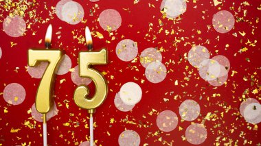Altın yanan mum numarası yetmiş beş. Kırmızı arkaplanda 75 yazılı doğum günü tebrik kartı konfeti ve simle. Yıldönümü, kutlama etkinliği ve doğum günü konsepti.