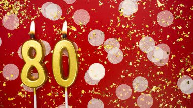 Altın yanan mum numarası seksen. Kırmızı arkaplanda 80 yazılı doğum günü tebrik kartı konfeti ve simle. Yıldönümü, kutlama etkinliği ve doğum günü konsepti.