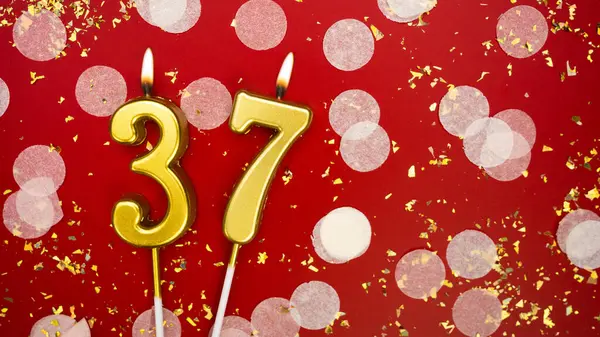 Altın yanan mum numarası otuz yedi. Kırmızı zemin üzerinde 37 yazısıyla konfeti ve simle birlikte doğum günü tebrik kartı. Yıldönümü, kutlama etkinliği ve doğum günü konsepti.