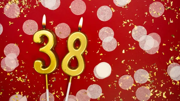 Altın yanan mum numarası otuz sekiz. Kırmızı zemin üzerinde 38 yazısıyla konfeti ve simle birlikte doğum günü tebrik kartı. Yıldönümü, kutlama etkinliği ve doğum günü konsepti.