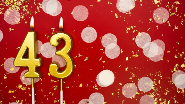 Altın yanan mum numarası kırk üç. Kırmızı arkaplanda 43 yazılı doğum günü tebrik kartı konfeti ve simle. Yıldönümü, kutlama etkinliği ve doğum günü konsepti.