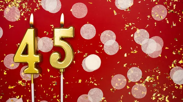Kırk beş numaralı altın yanan mum. Kırmızı arkaplanda 45 yazılı doğum günü tebrik kartı konfeti ve simle. Yıldönümü, kutlama etkinliği ve doğum günü konsepti.