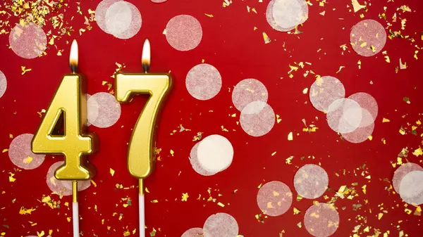 Kırk yedi numaralı altın yanan mum. Kırmızı arka planda 47 yazılı konfeti ve simli doğum günü tebrik kartı. Yıldönümü, kutlama etkinliği ve doğum günü konsepti.