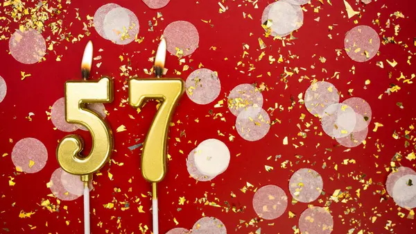 Elli yedi numaralı altın yanan mum. Kırmızı arkaplanda 57 yazılı doğum günü tebrik kartı konfeti ve simle. Yıldönümü, kutlama etkinliği ve doğum günü konsepti.
