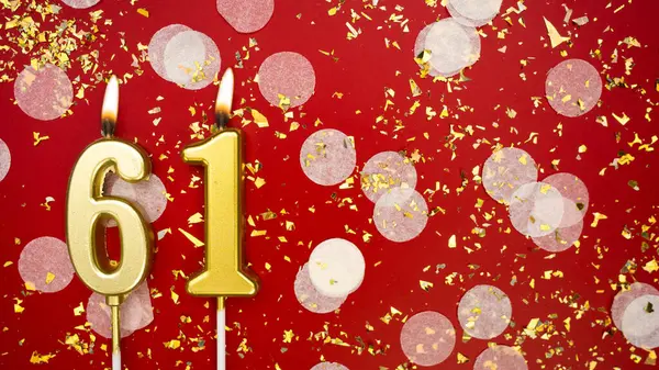 Altın yanan mum numarası 61 'di. Kırmızı arka planda 61 yazısıyla konfeti ve simle birlikte doğum günü tebrik kartı. Yıldönümü, kutlama etkinliği ve doğum günü konsepti.
