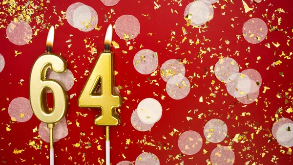 Altmış dört numaralı altın yanan mum. Kırmızı arkaplanda 64 yazılı doğum günü tebrik kartı konfeti ve simle. Yıldönümü, kutlama etkinliği ve doğum günü konsepti.