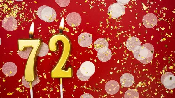 Yetmiş iki numaralı altın yanan mum. Kırmızı arka planda 72 yazısıyla konfeti ve simle birlikte doğum günü tebrik kartı. Yıldönümü, kutlama etkinliği ve doğum günü konsepti.