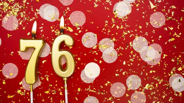 Altın yanan mum numarası 76 'dır. Kırmızı arka planda 76 yazısıyla birlikte konfeti ve simle birlikte doğum günü tebrik kartı. Yıldönümü, kutlama etkinliği ve doğum günü konsepti.