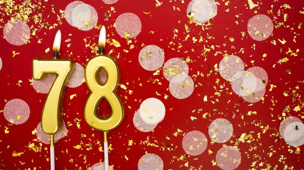 Altın yanan mum numarası 78 'di. Kırmızı zemin üzerinde 78 yazısıyla konfeti ve simle birlikte doğum günü tebrik kartı. Yıldönümü, kutlama etkinliği ve doğum günü konsepti.