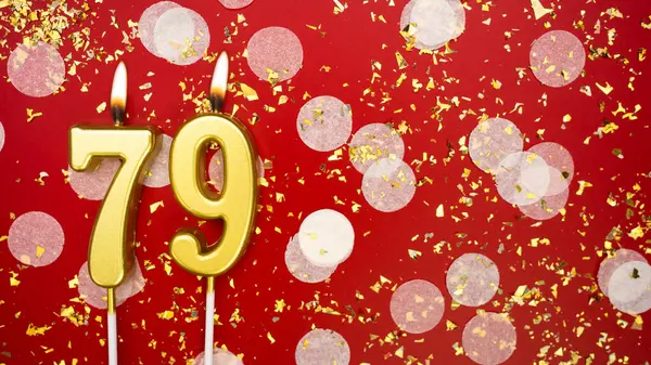 Altın yanan mum numarası 79 'du. Kırmızı arkaplanda 79 yazılı doğum günü tebrik kartı konfeti ve simle. Yıldönümü, kutlama etkinliği ve doğum günü konsepti.