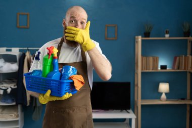 Temizlik sepetinde temizlik malzemesi olan hizmetli şaşırmış ve şaşırmış bir yüz ifadesi sergiliyor ya da oturma odasında dururken dağıtıyor. Boşluğu kopyala