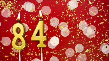 Seksen dört numaralı altın yanan mum. Kırmızı arka planda 84 yazısıyla birlikte konfeti ve simle birlikte doğum günü tebrik kartı. Yıldönümü, kutlama etkinliği ve doğum günü konsepti.