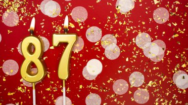 Seksen yedi numaralı altın yanan mum. Kırmızı arkaplanda 87 yazılı doğum günü tebrik kartı konfeti ve simle. Yıldönümü, kutlama etkinliği ve doğum günü konsepti.