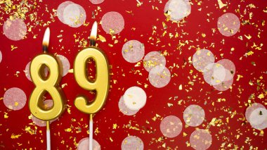 Altın yanan mum numarası seksen dokuz. Kırmızı zemin üzerinde 89 yazısıyla konfeti ve simle birlikte doğum günü tebrik kartı. Yıldönümü, kutlama etkinliği ve doğum günü konsepti.