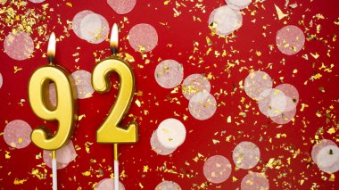 Altın yanan mum numarası 92 'ydi. Kırmızı arkaplanda 92 yazılı doğum günü tebrik kartı konfeti ve simle. Yıldönümü, kutlama etkinliği ve doğum günü konsepti.