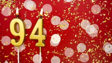 Altın yanan mum numarası 94 'tü. Kırmızı arka planda 94 yazısıyla birlikte konfeti ve simle birlikte doğum günü tebrik kartı. Yıldönümü, kutlama etkinliği ve doğum günü konsepti.