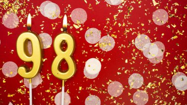 Altın yanan mum numarası 98 'di. Kırmızı arkaplanda 98 yazılı doğum günü tebrik kartı konfeti ve simle. Yıldönümü, kutlama etkinliği ve doğum günü konsepti.