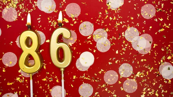 Altın yanan mum numarası 86 'ydı. Kırmızı arka planda 86 yazısıyla konfeti ve simle birlikte doğum günü tebrik kartı. Yıldönümü, kutlama etkinliği ve doğum günü konsepti.