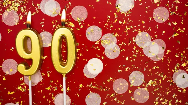Altın yanan mum numarası 90. Kırmızı arkaplanda 90 yazılı doğum günü tebrik kartı konfeti ve simle. Yıldönümü, kutlama etkinliği ve doğum günü konsepti.