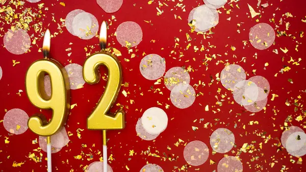 Altın yanan mum numarası 92 'ydi. Kırmızı arkaplanda 92 yazılı doğum günü tebrik kartı konfeti ve simle. Yıldönümü, kutlama etkinliği ve doğum günü konsepti.
