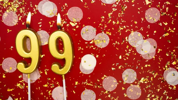 Altın yanan mum numarası 99 'du. Kırmızı arka planda 99 yazısıyla birlikte konfeti ve simle doğum günü tebrik kartı. Yıldönümü, kutlama etkinliği ve doğum günü konsepti.