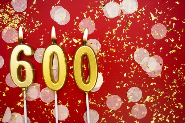 Kırmızı konfeti arka planında yanan altın doğum günü mumları, 600. kopya alanı