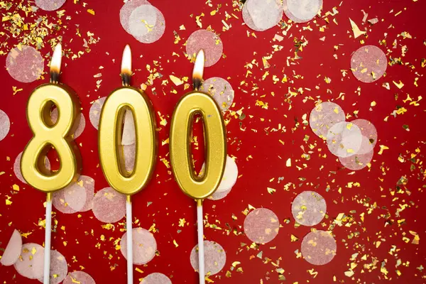 Kırmızı konfeti arka planında yanan altın doğum günü mumları, numara 800. Kopyalama alanı