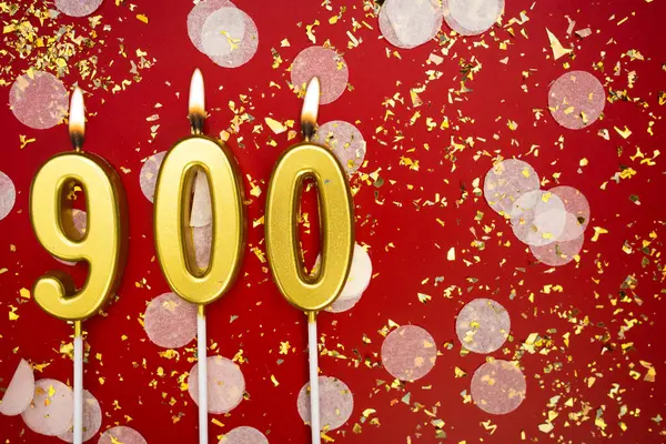 Kırmızı konfeti arka planında yanan altın doğum günü mumları, numara 900. kopyalama alanı