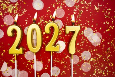 Mutlu yıllar 2027. Tatil geçmişi. 2027 yılının sayıları kırmızı arka planda konfeti ve simle altın mum yakmaktan. Yeni yıl tatili kavramı. Boşluğu kopyala