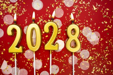 Mutlu yıllar 2028. Tatil geçmişi. 2028 yılının sayıları kırmızı arka planda konfeti ve simle yanan altın mumlardan geliyor. Yeni yıl tatili kavramı. Boşluğu kopyala