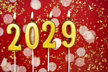Mutlu yıllar 2029. Tatil geçmişi. 2029 yılının sayıları kırmızı arka planda konfeti ve simle yanan altın mumlardan geliyor. Yeni yıl tatili kavramı. Boşluğu kopyala